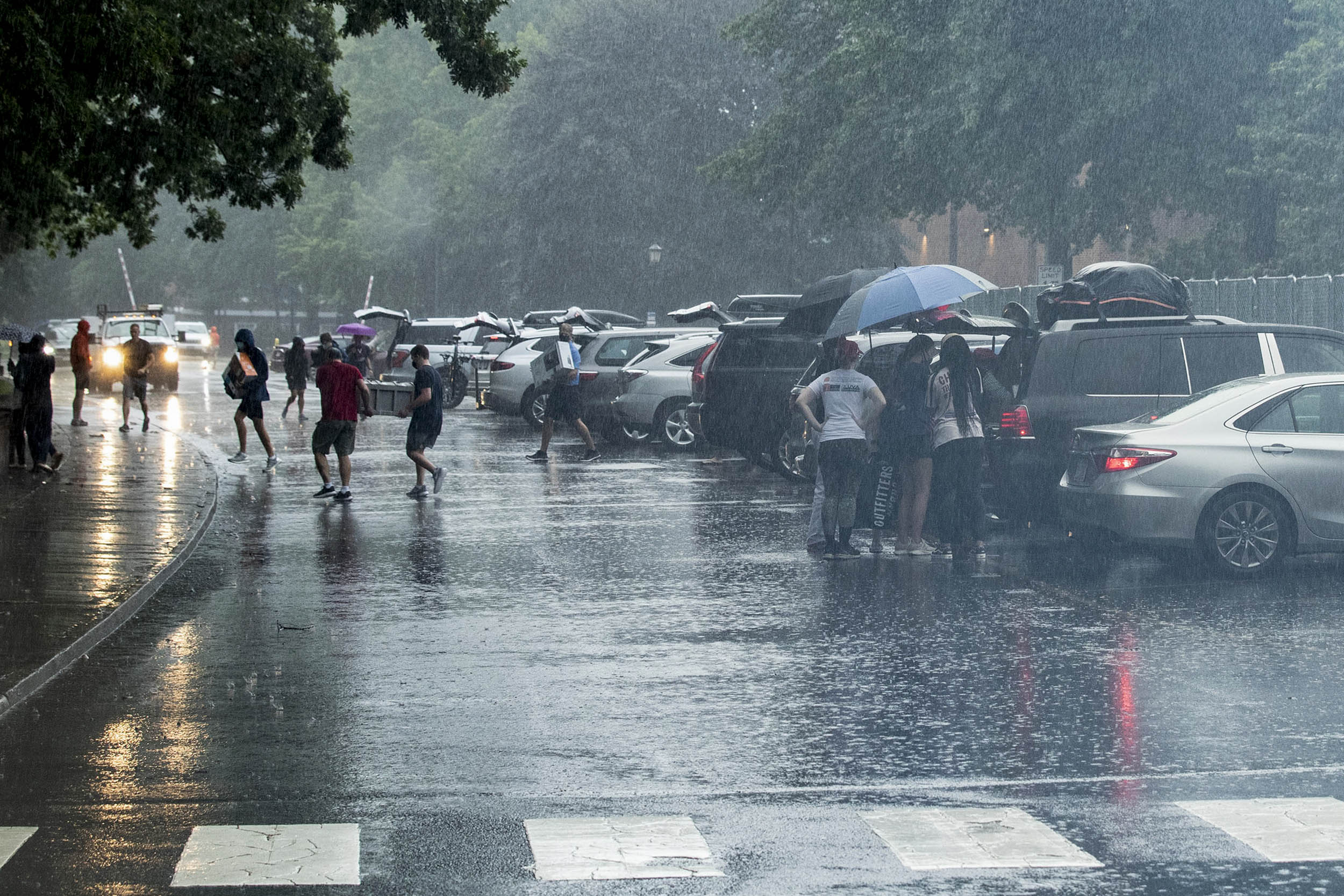 Families and students with umbrellas move personal belongings into a dorm