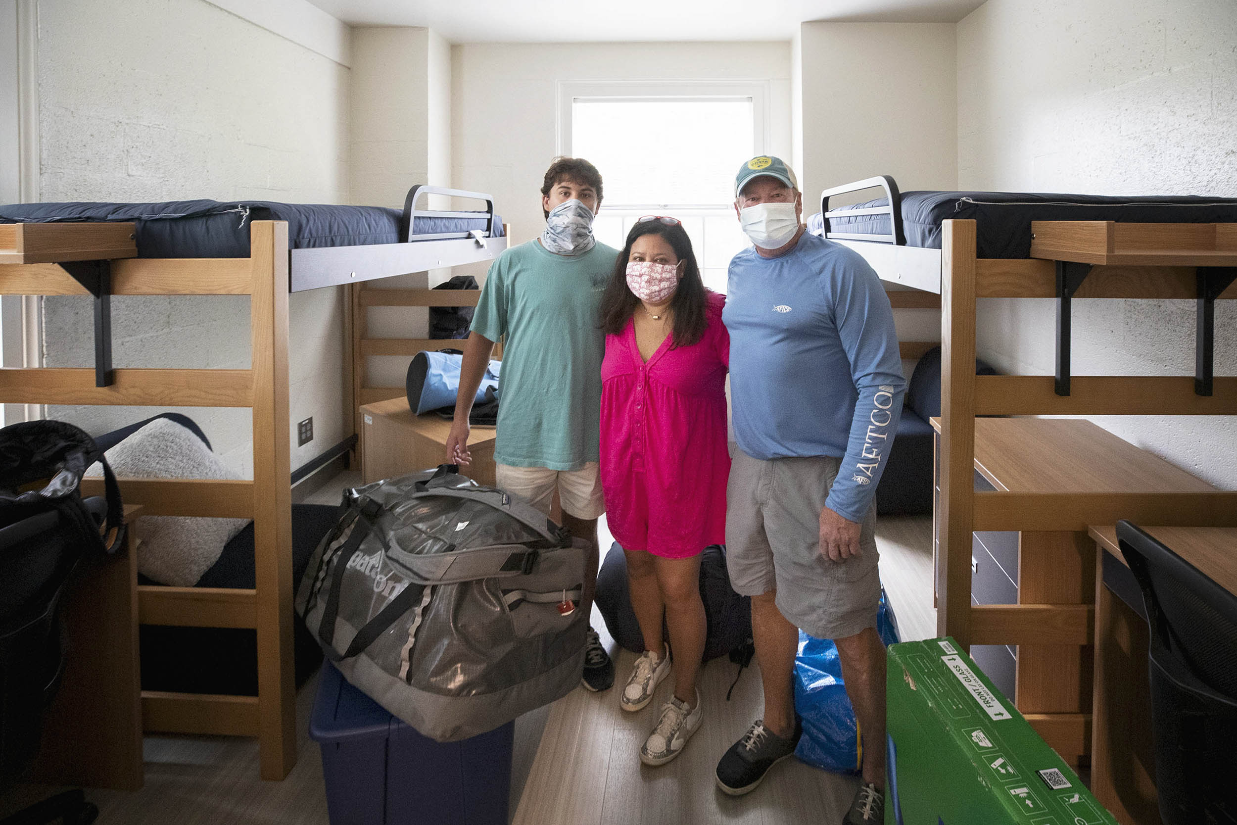 Student and family in their dorm room posing for a picture together with boxes and luggage around