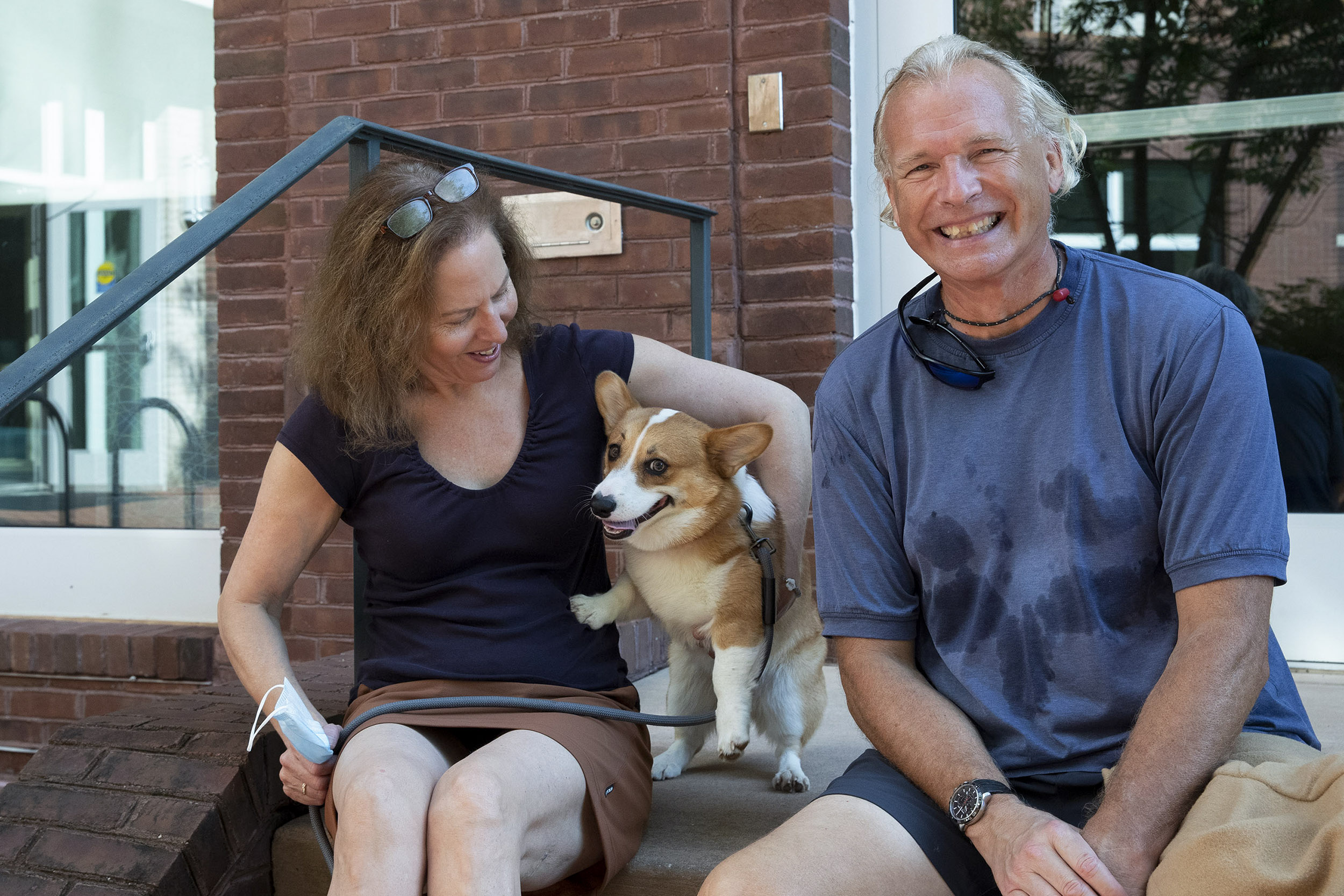 Two people sitting on a dorms steps with a dog