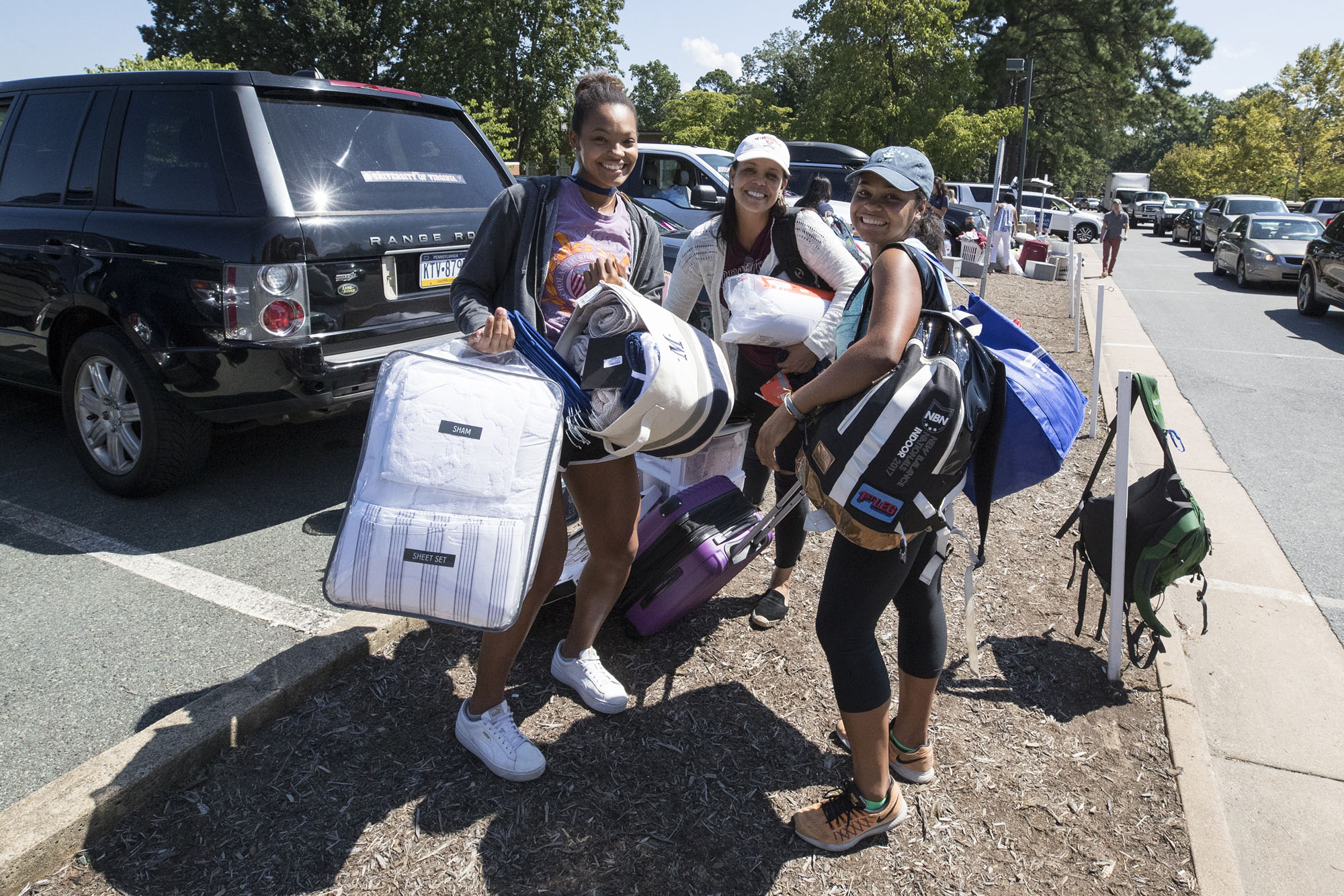 Group of students stand together holding their belongings as they prepare to move into their rooms