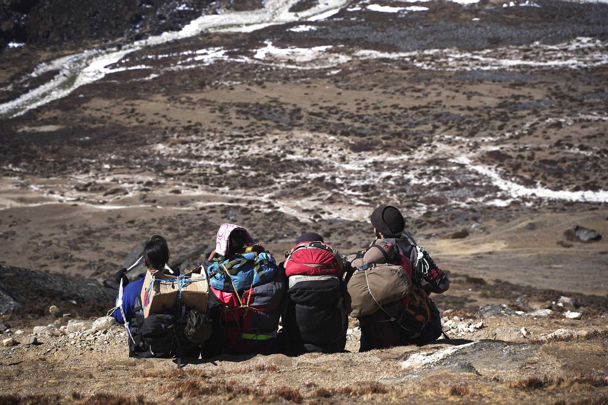four people sitting on the ground looking down from a Himalayan mountain