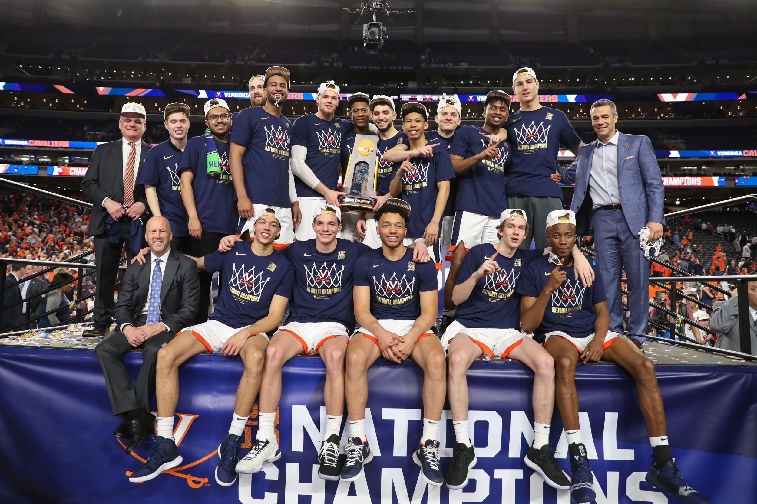 UVA basketball team sitting and standing on the Final Four stage holding the NCAA trophy