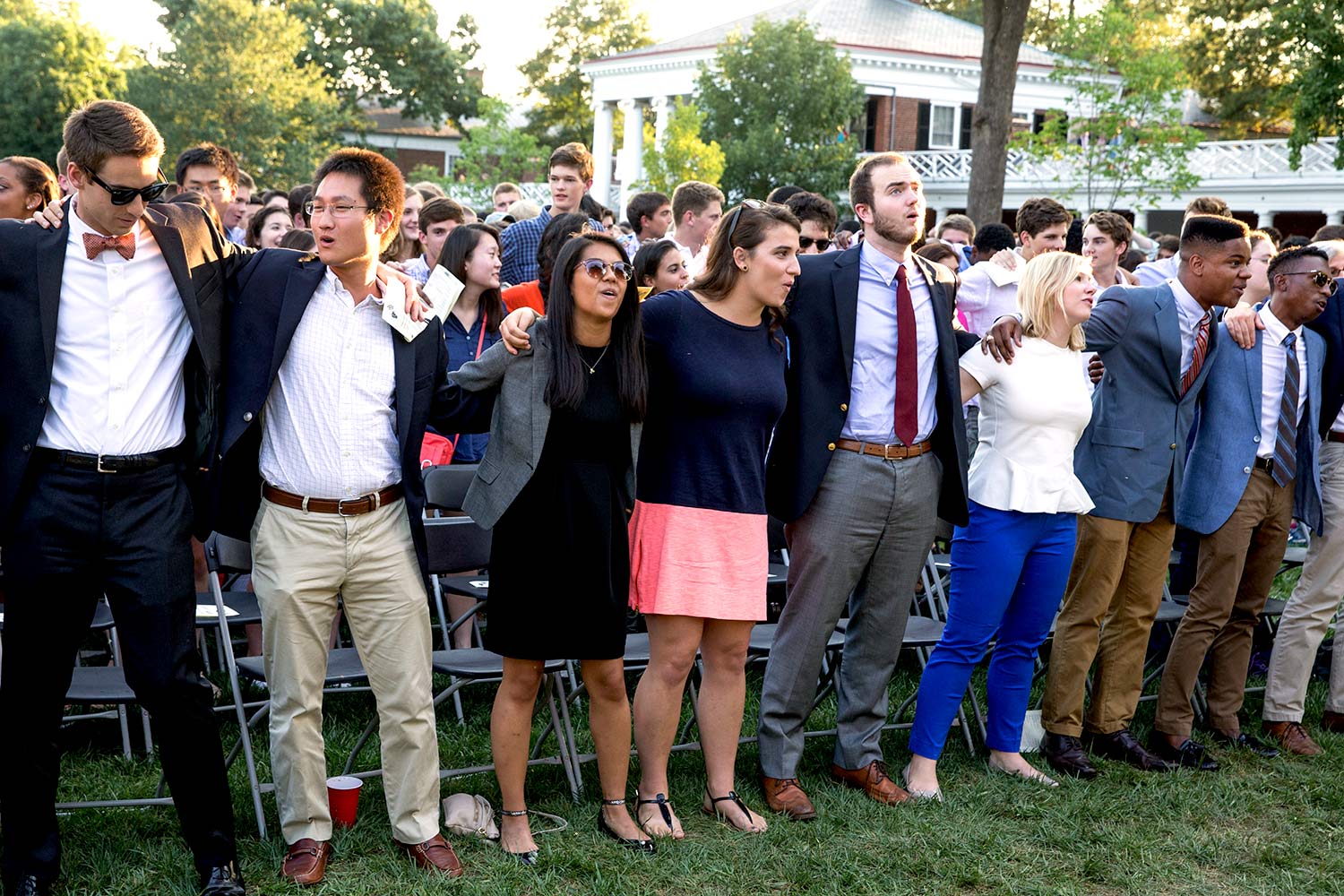 Students with arms wrapped around each other singing on the lawn during opening convocation