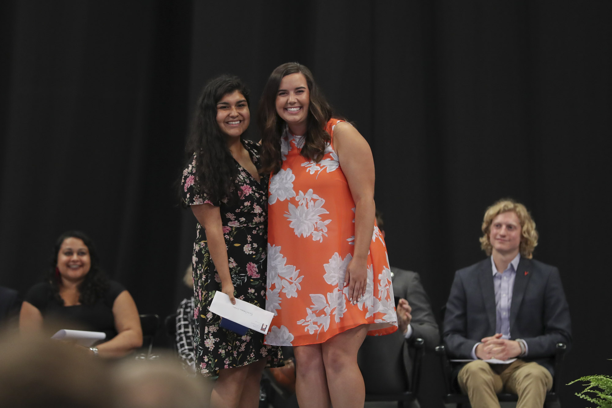Holly Stevens, right, and Paola Sanchez Valdez, left, stand on stage smiling at the camera