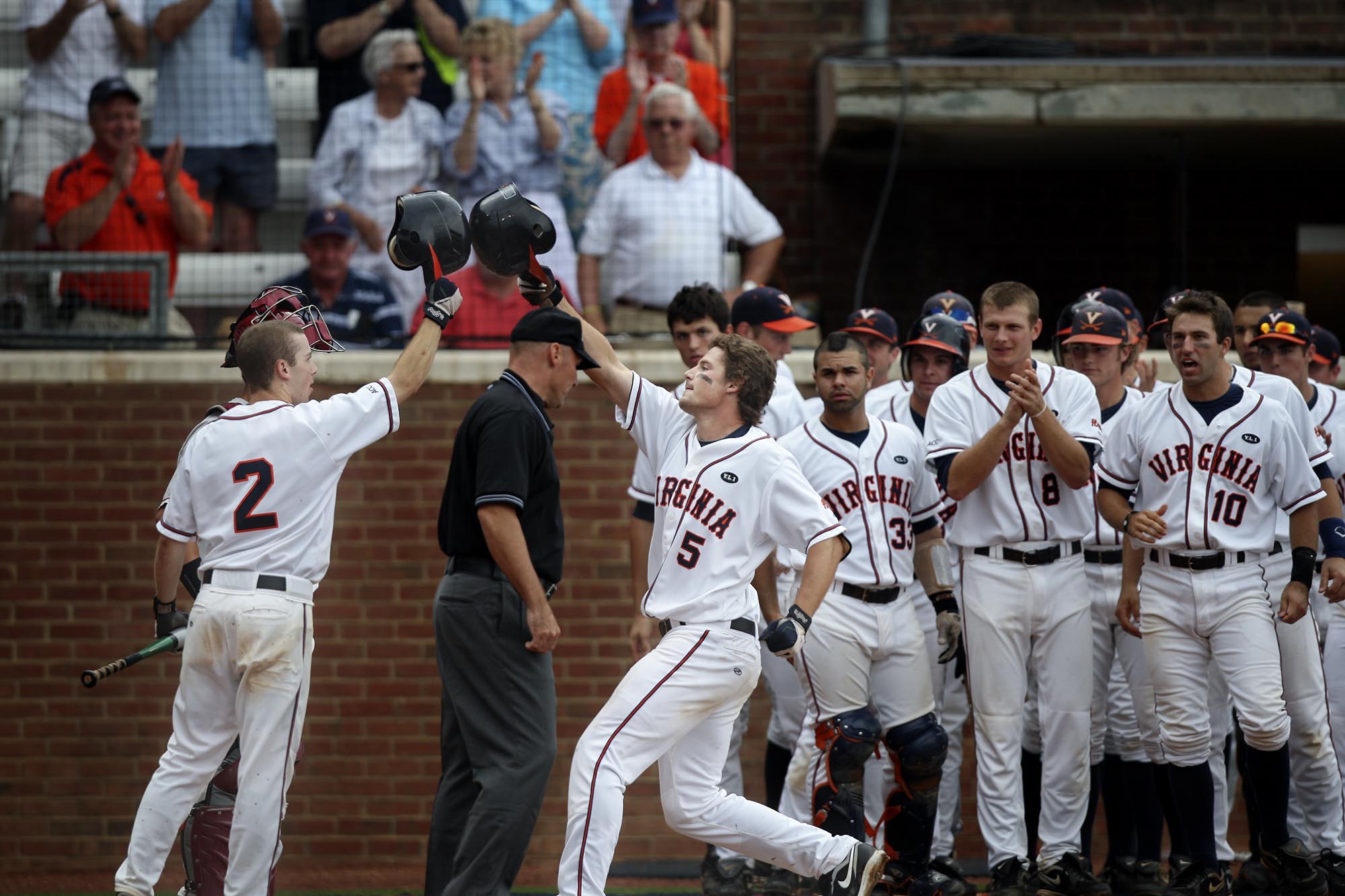 UVA Baseball team standing at the dugout entrance clapping while two players raise their helmets towards each other