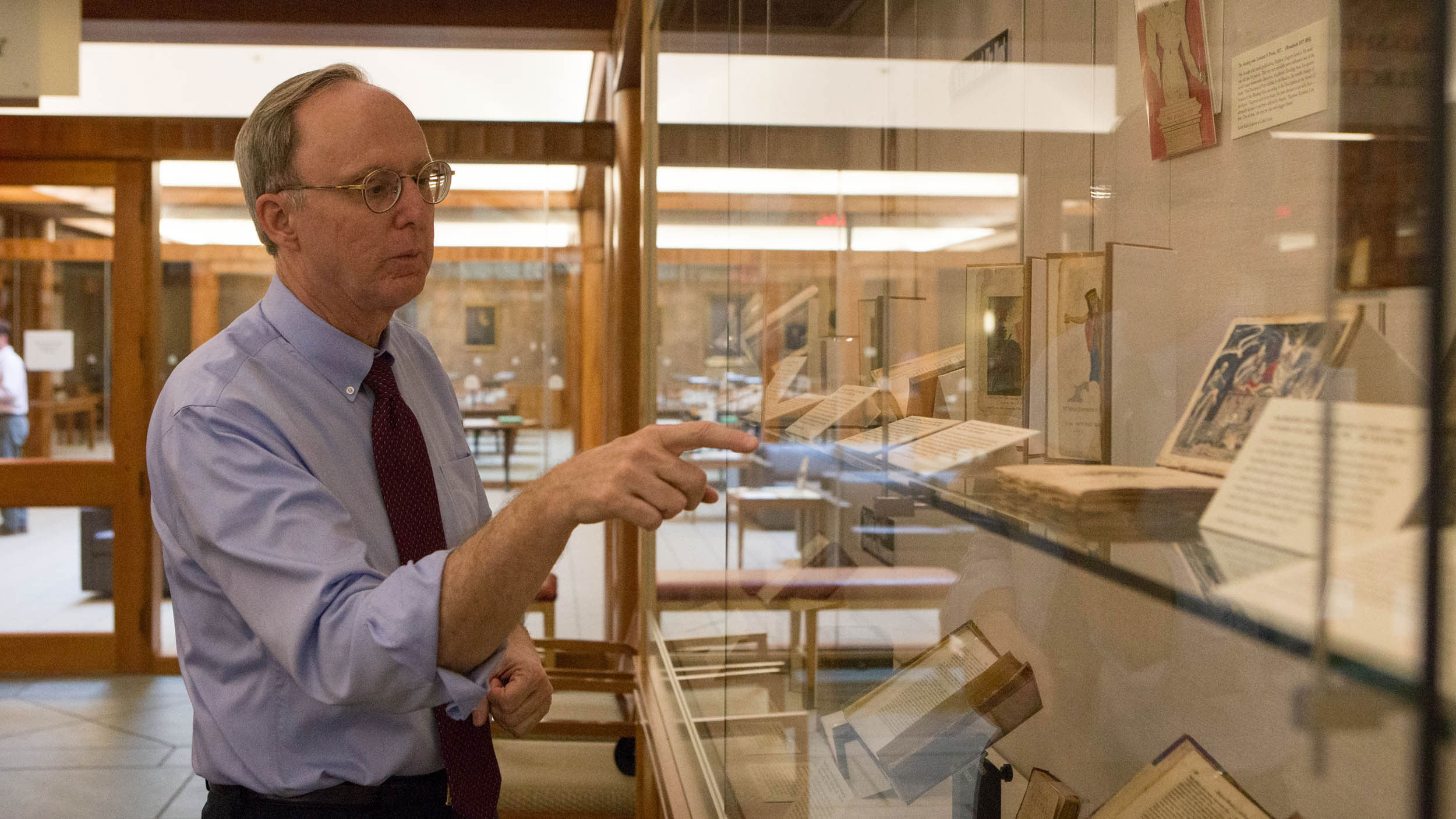 Man pointing to a glass case with old books in them talking