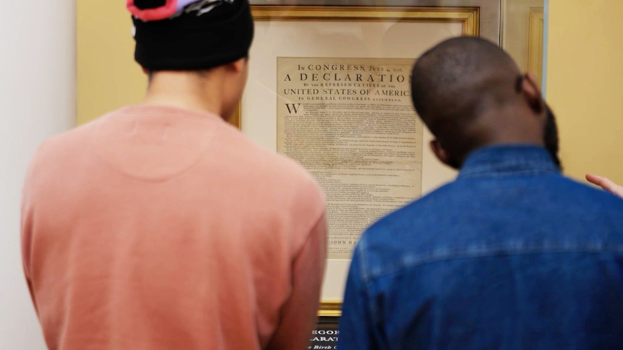 From over the shoulder of two people looking at an original copy of the Declaration of Independence