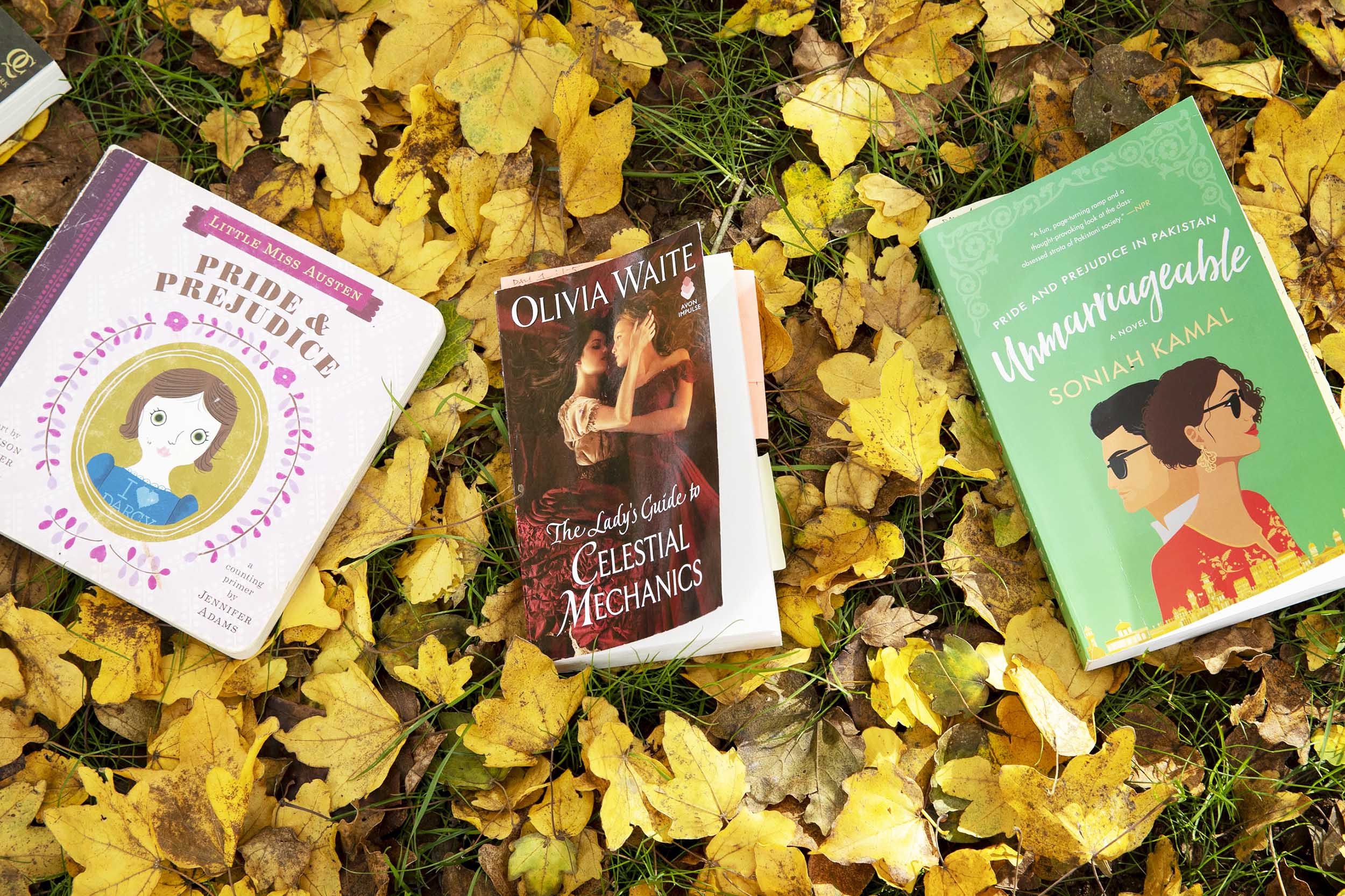 Three books laying in yellow leaves.  Left to Right: Little Miss Austen Pride & Prejudice, Olivia Waite The Lady's Guide to Celestial Mechanics, and Unmarriageable