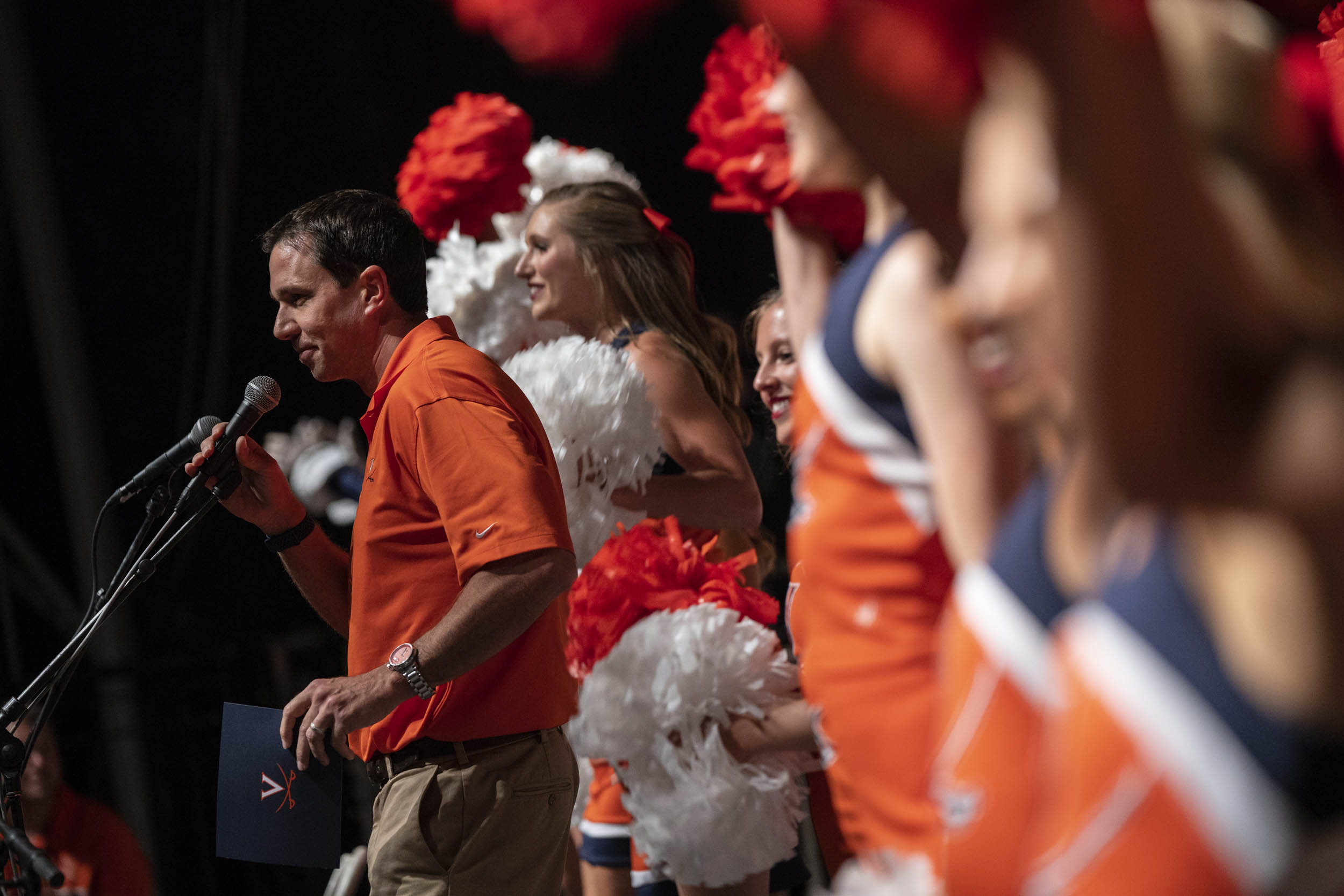 Cheerleaders on stage with a man talking into a microphone