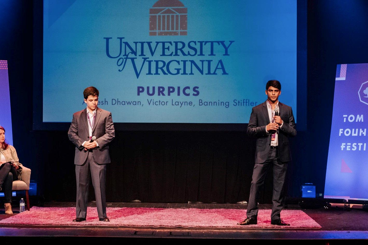 Layne, left, and Dhawan stand on stage making a presentation