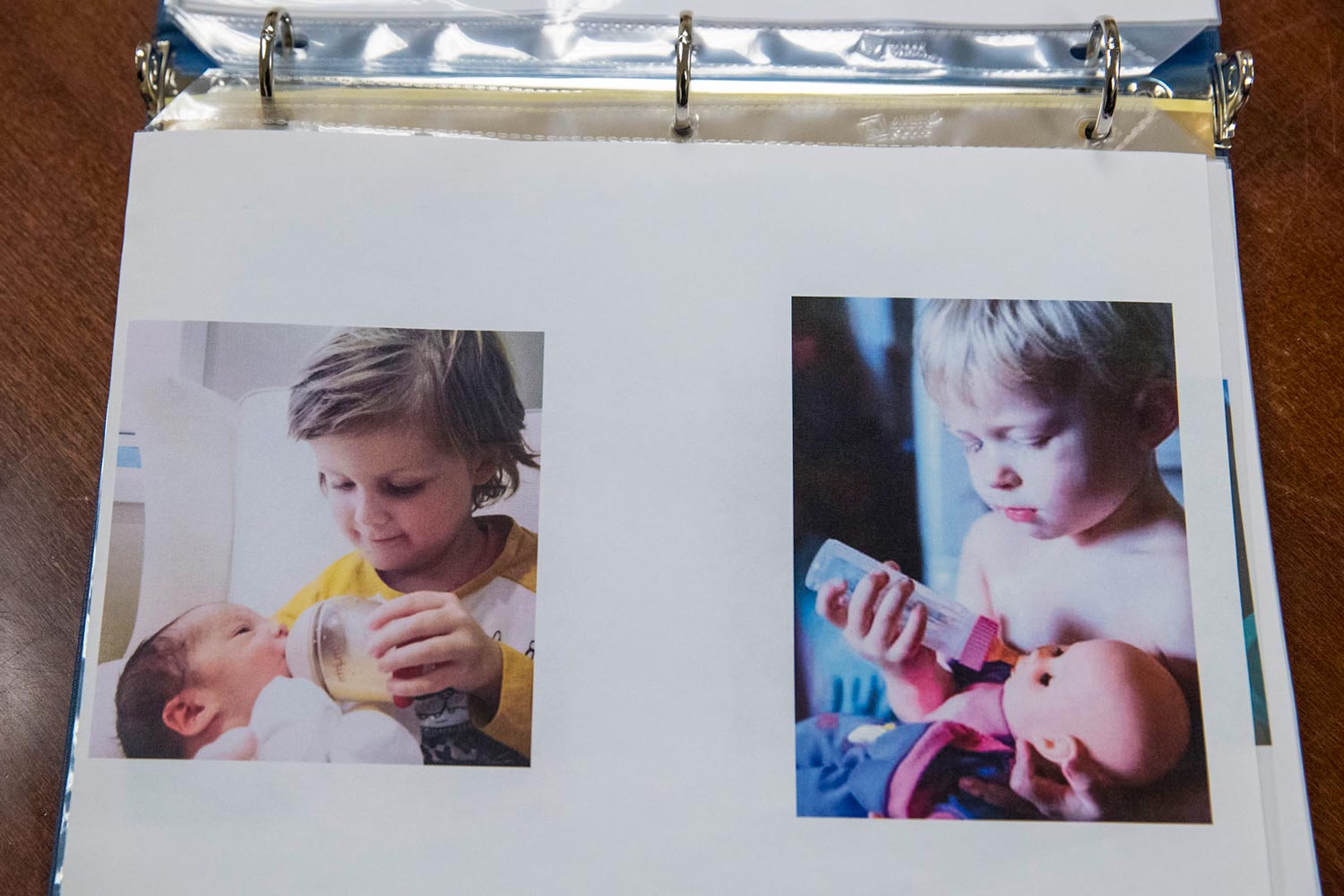 Two photos in a binder: a small child bottle-feeding a baby, and a small child bottle-feeding a doll