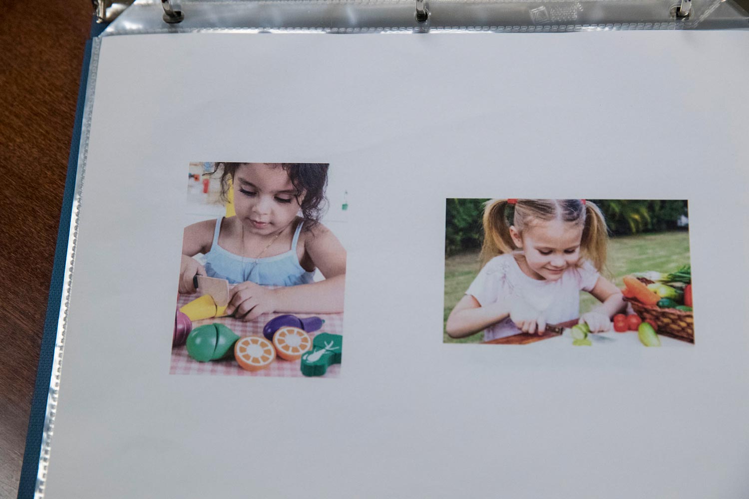 Two photos in a binder: a small child cutting a toy vegetable with a toy knife, and a small child cutting a real vegetable with a real knife.