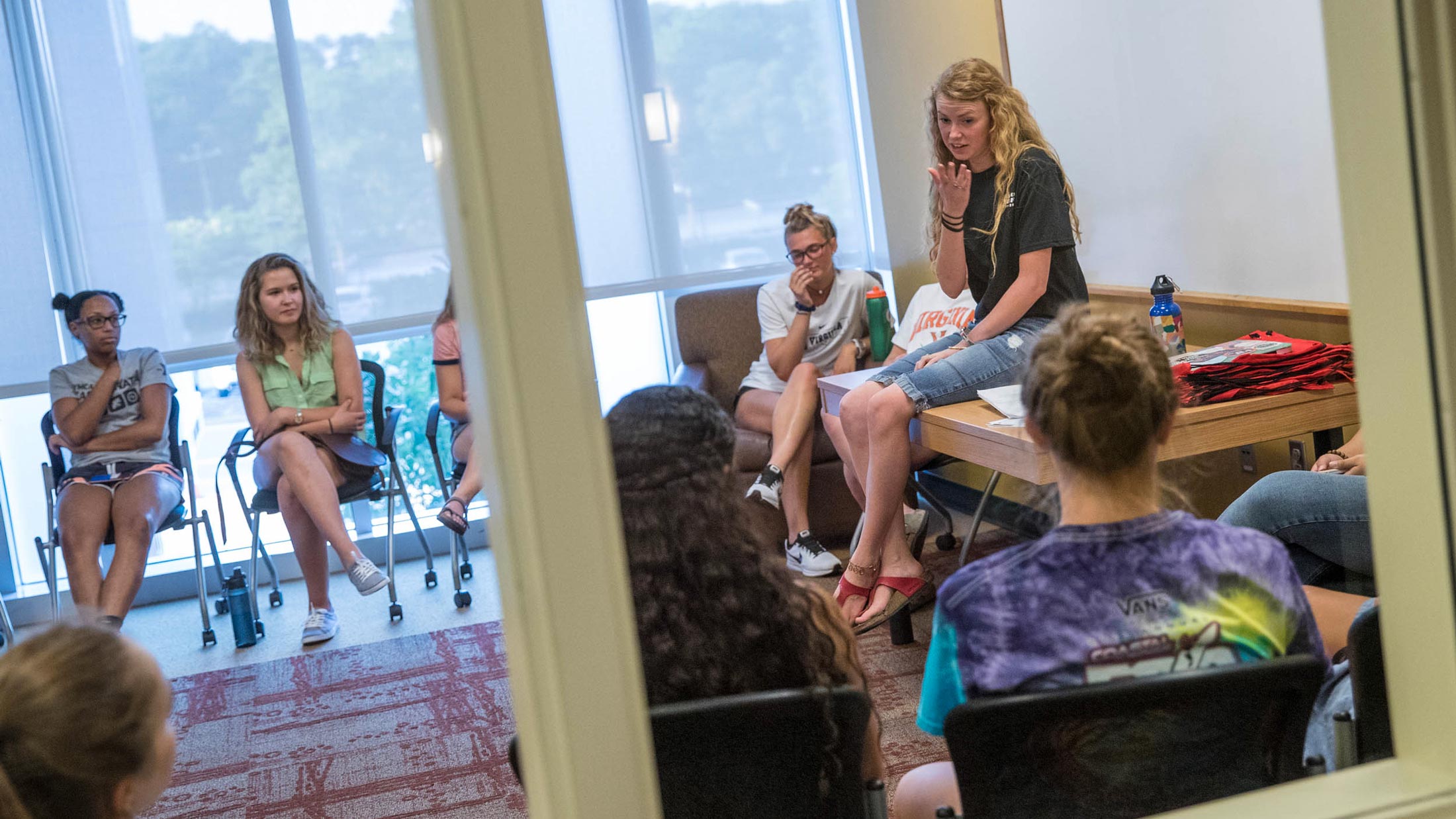 Rebecca Lewis sits on a table and talks to fellow students  who are sitting in chairs in a circle