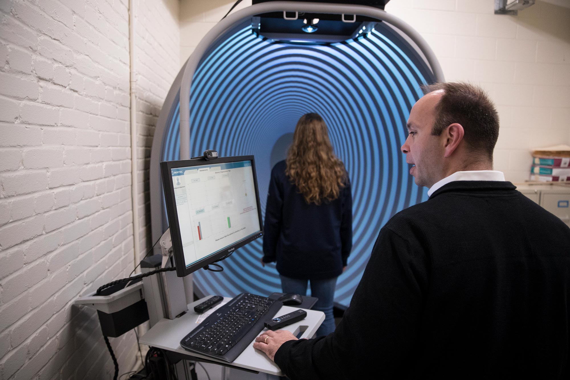 acob Resch,works on a computer while Erika Osherow stands in front of a screen that has dark blue and light blue circles 