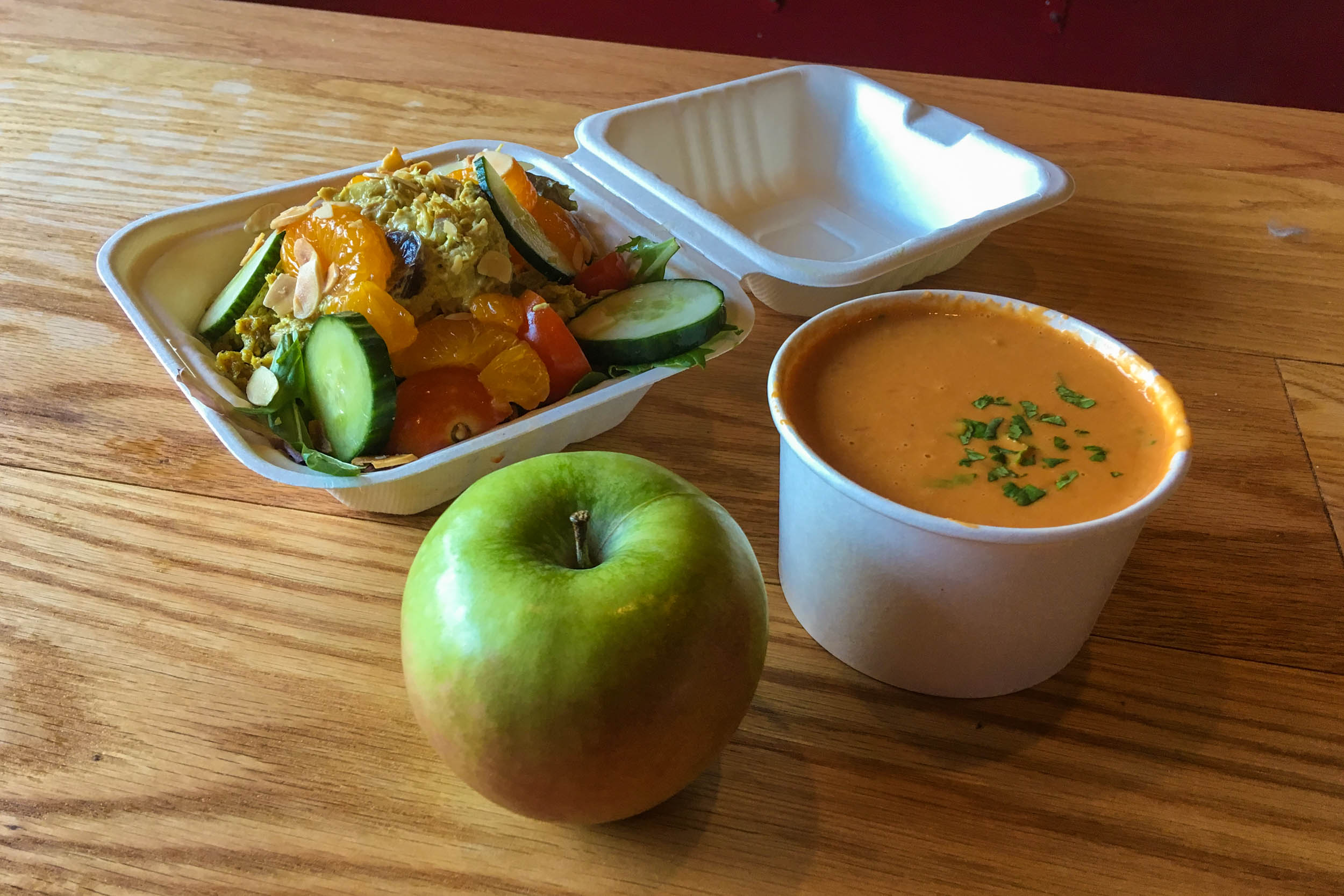 Salad in a box, an apple, and a bowl of soup