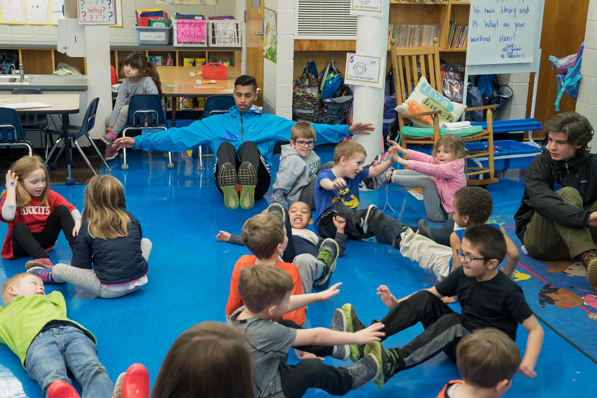 Small children and adults sit on the floor and hold their feet and arms up in partner groups