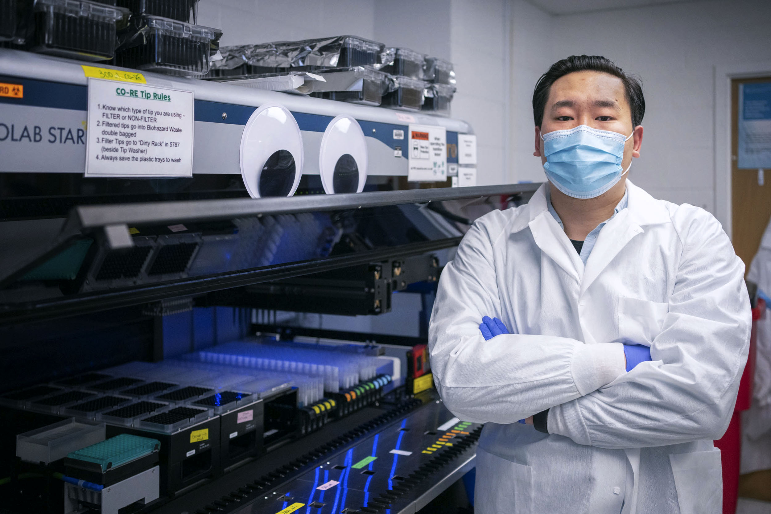 Pu (Bruce) Zhang standing in a lab next to saliva testing machine
