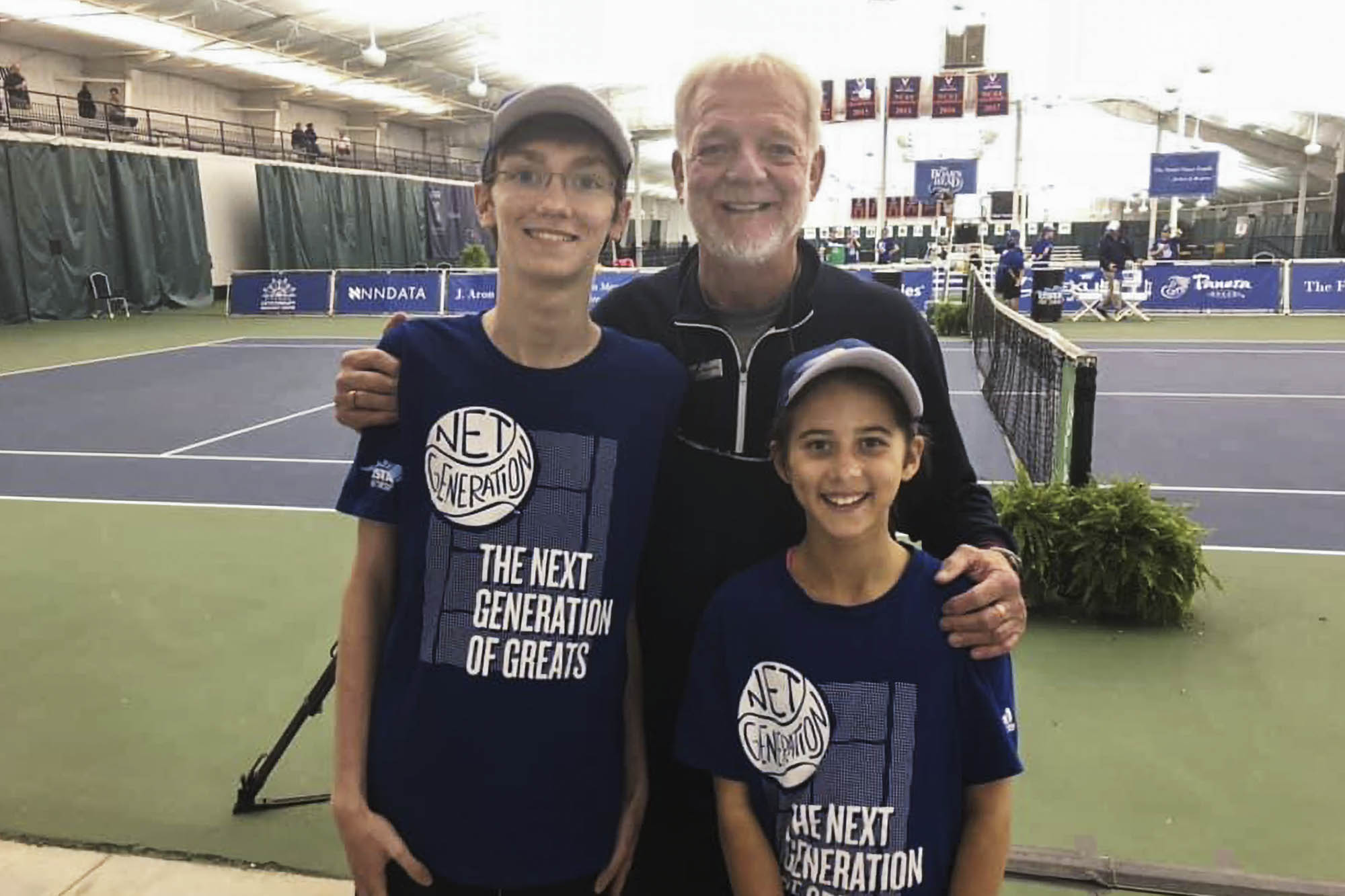 Manilla standing on a tennis court with two youth in front of him