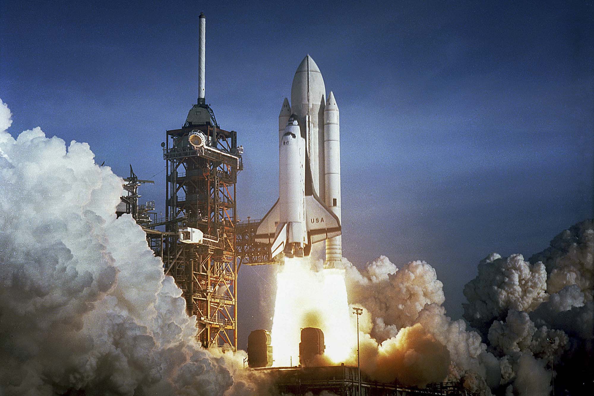 The Space Shuttle Columbia launching into the air with grey smoke surround it and bright white and yellow flames coming out the bottom