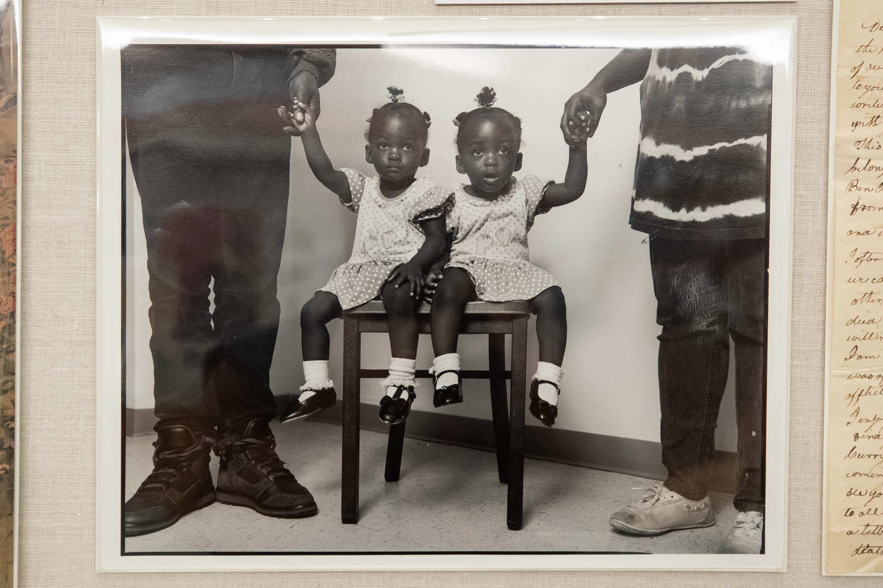 two little African American girls sit on a chair together while two adults hold their hands