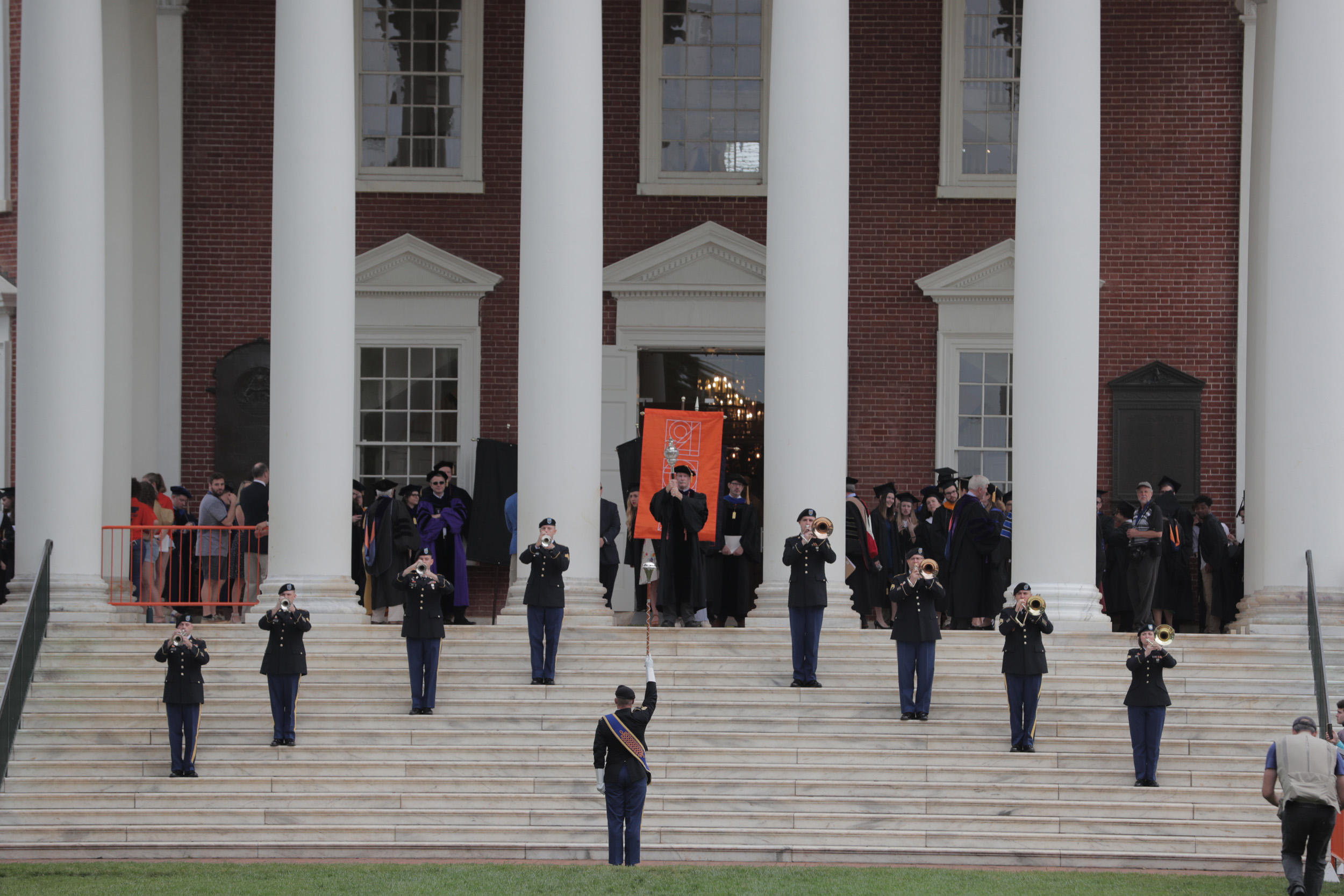 Military members stand on the steps of the Rotunda playing trumpets while graduates walk down the Rotunda steps