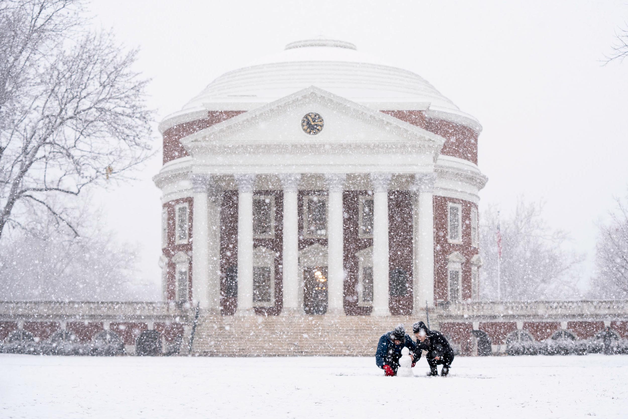 Two people building a small snowman in front of the Rotunda