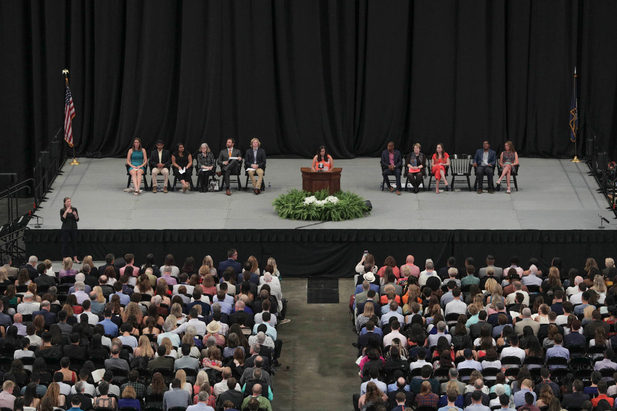 Students and presenters on stage with one speaking to a crowd from the podium
