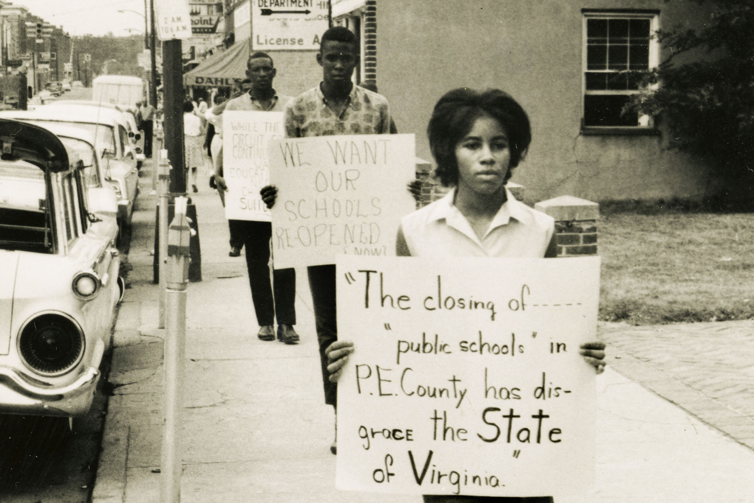 African Americans protesting on a public street with a sign that reads: the closing of public schools in p.e. county has Disgrace the state of Virginia