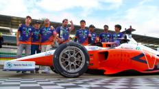 The race car team stands behind the car