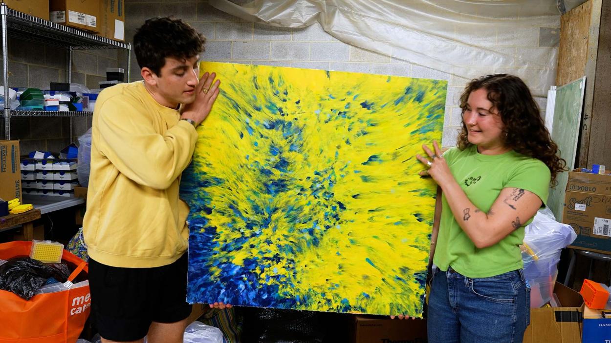 Two students displaying a piece of art created from trash.