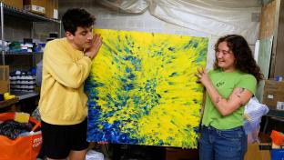 Two students displaying a piece of art created from trash.