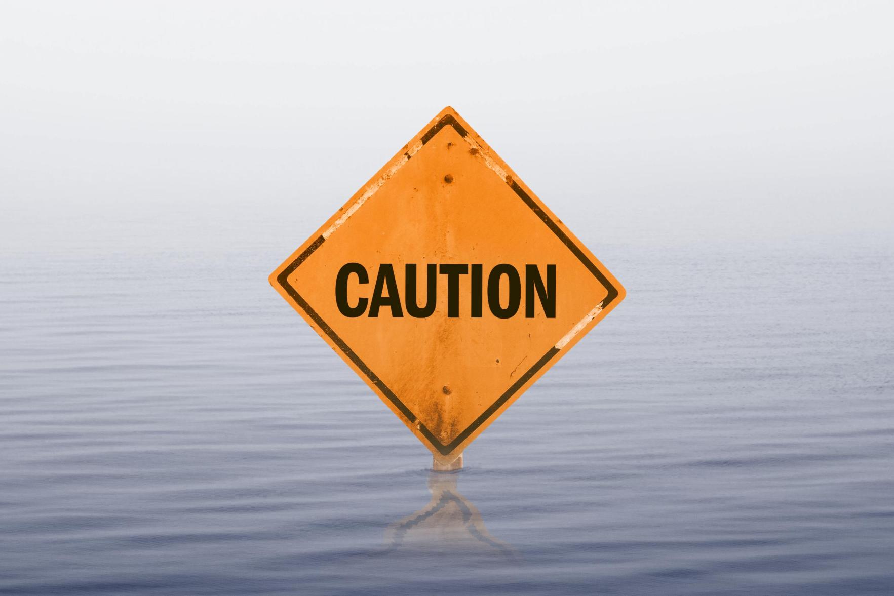 a diamond-shaped caution road sign is barely visible in rising flood water