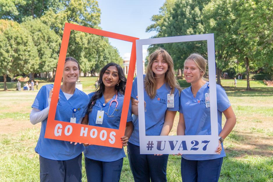 Four students holding up signs that say "Go Hoos" and "#uva 27"