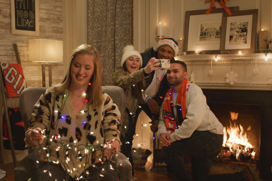 Three students in front of a fire place taking a selfie while another student sits in a chair detangling lights