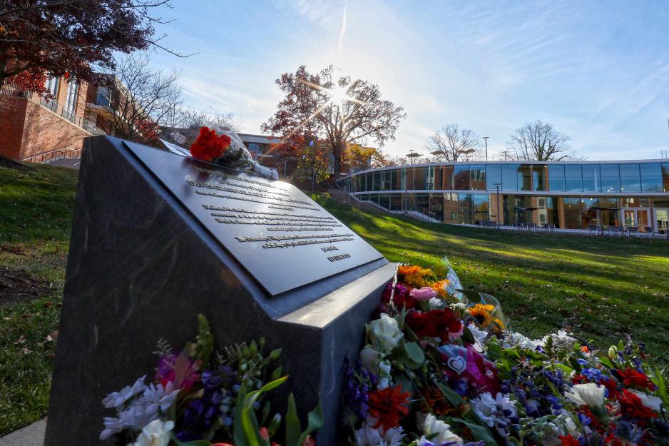 a memorial statue on UVA grounds with several bouquets of flowers laid around it