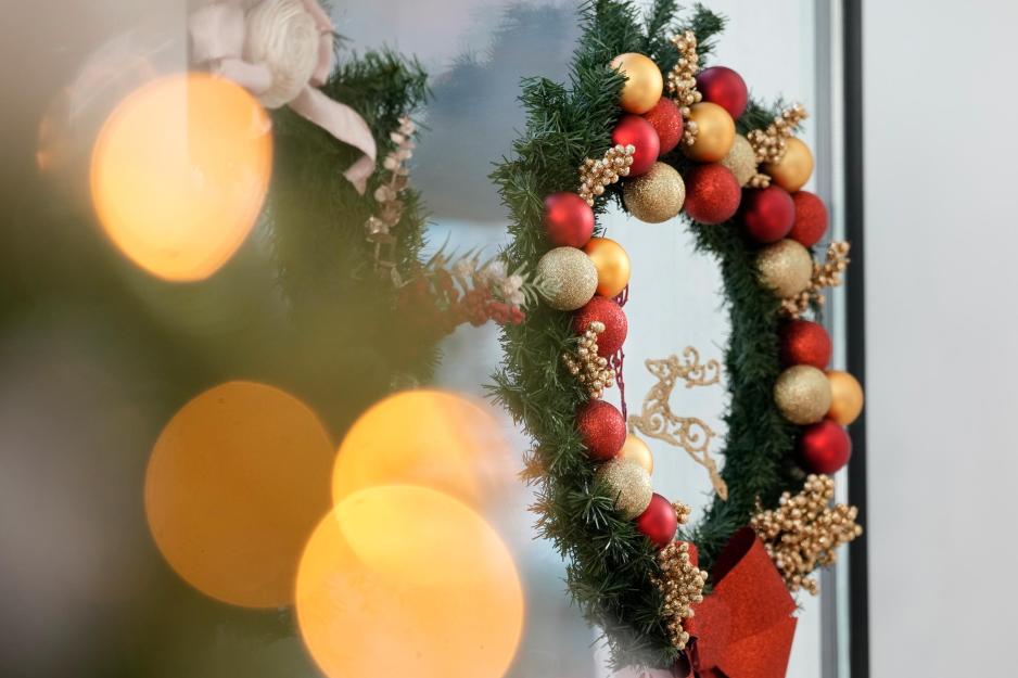 A portrait of a door decorated with lights and a hanging Christmas wreath.