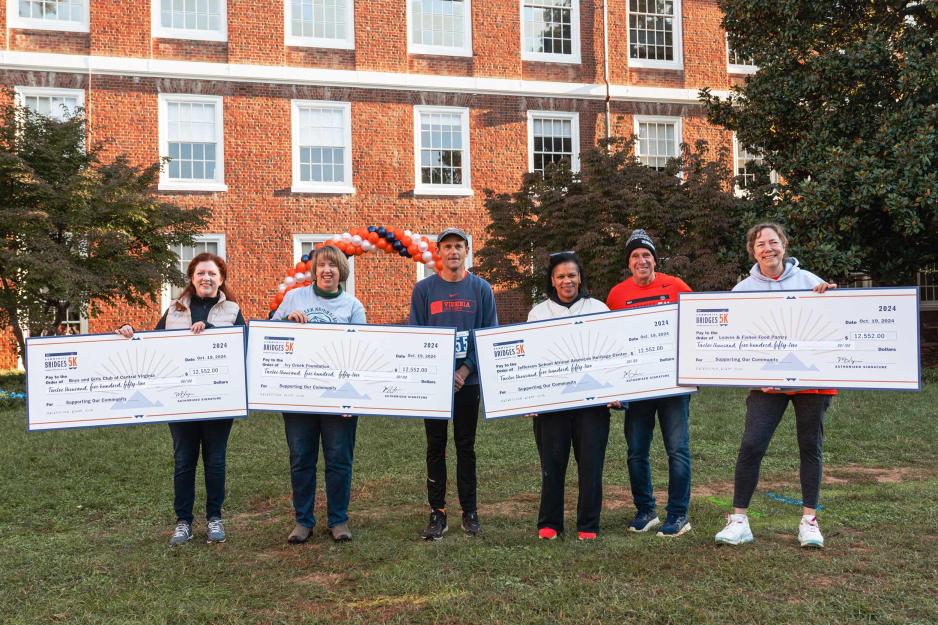 President Jim RYan and others stand and hold 4 giant checks