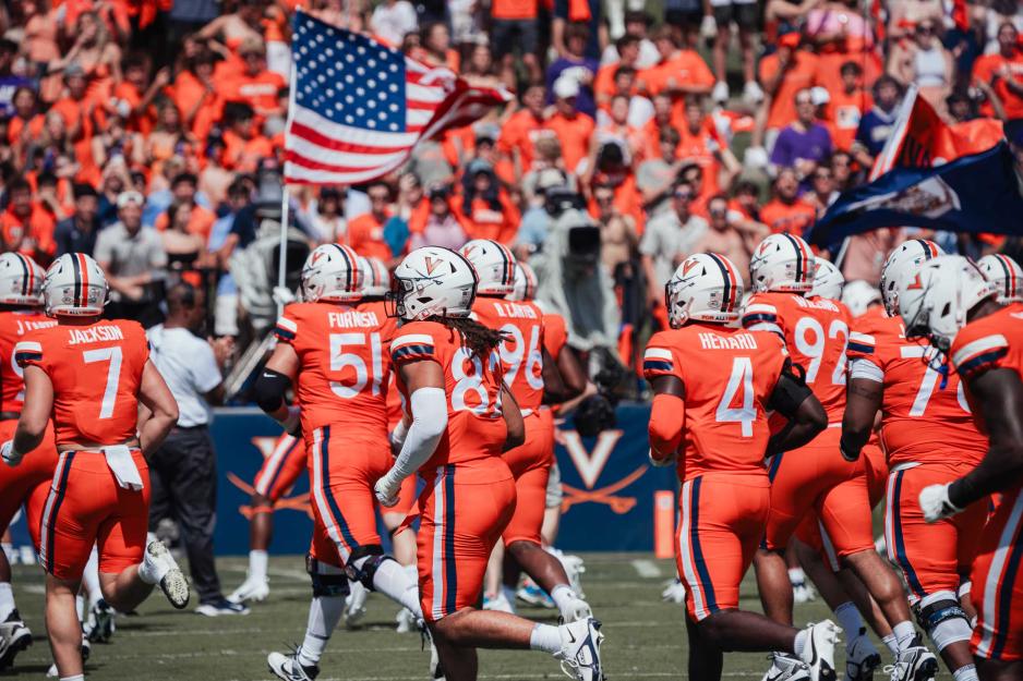 UVA football players run out onto the field carrying a US flag