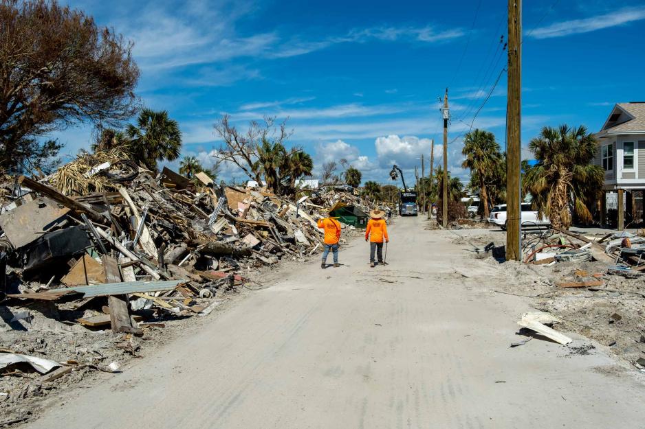 Two people walk down a road examining hurricane destruction