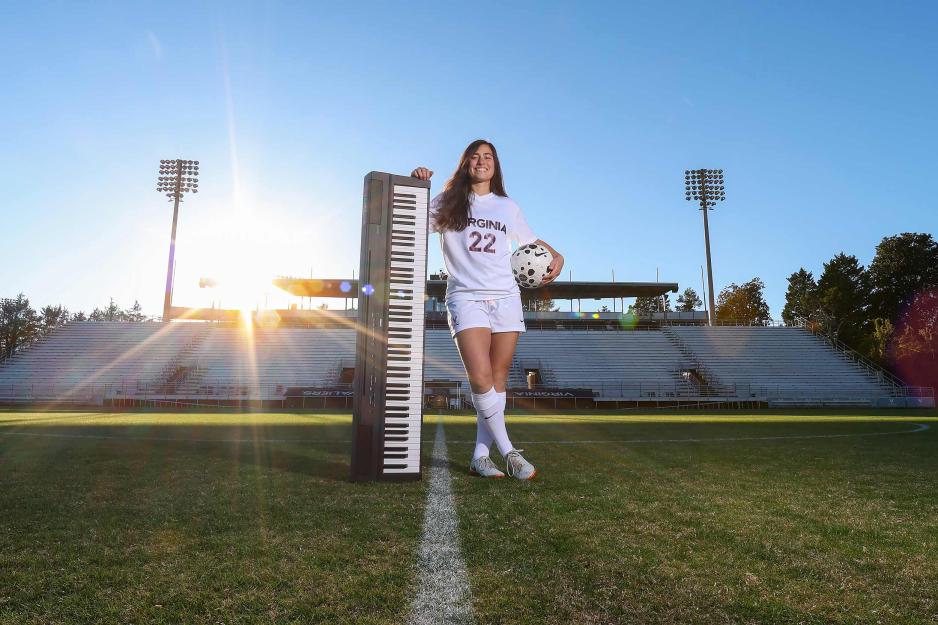 Lia Godfrey holding a digital piano with the edge on the soccer field as the sun sets behind the bleachers.
