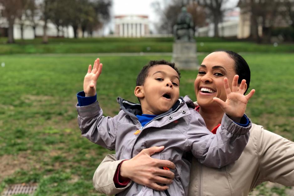 Portrait of UVA alumna Linsey Davis holding her son, with The Rotunda and UVA Lawn in the background.