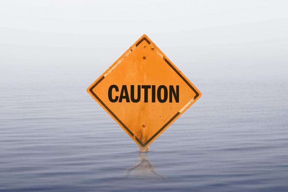 a diamond-shaped caution road sign is barely visible in rising flood water