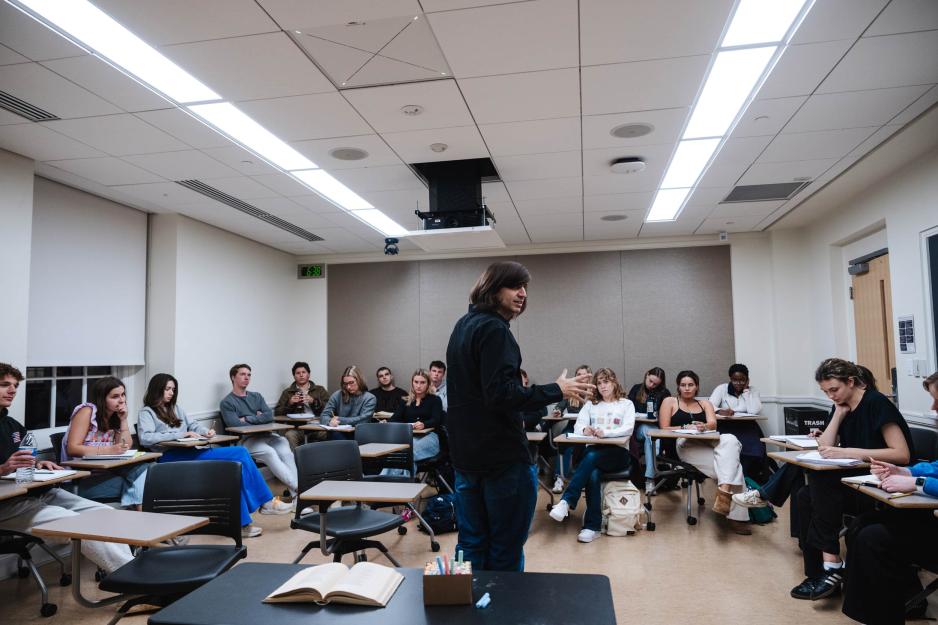 Students sitting in a classroom while a professor stands in the center to teach