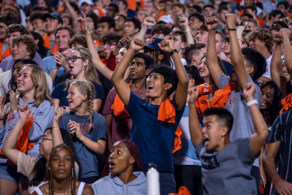 College students in blue and orange clothing cheer from the stands