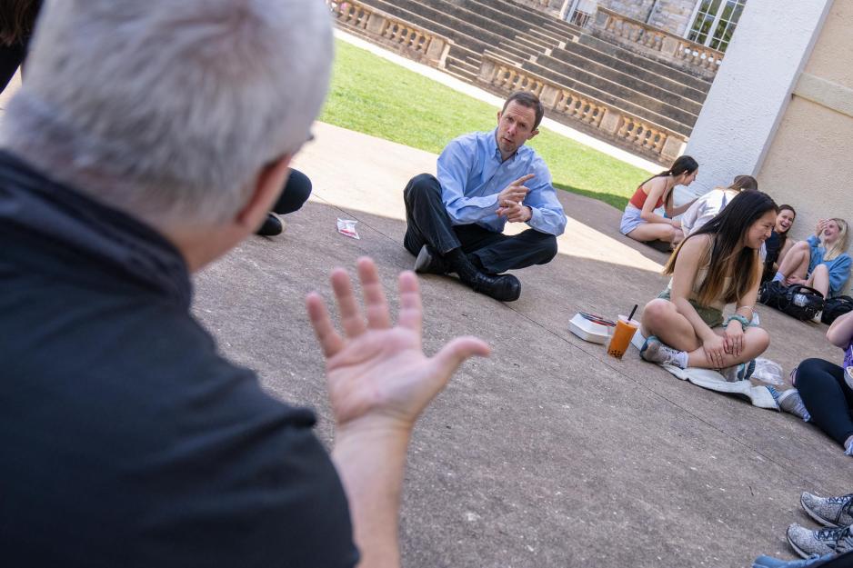 Christopher Krentz sits cross-legged on the ground in a circle of people eating lunch and communicating in American Sign Language