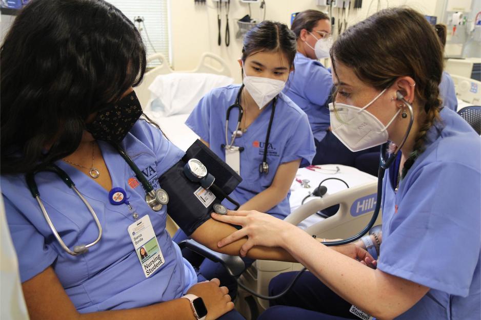 Three nursing students practice taking one another's blood pressure. 