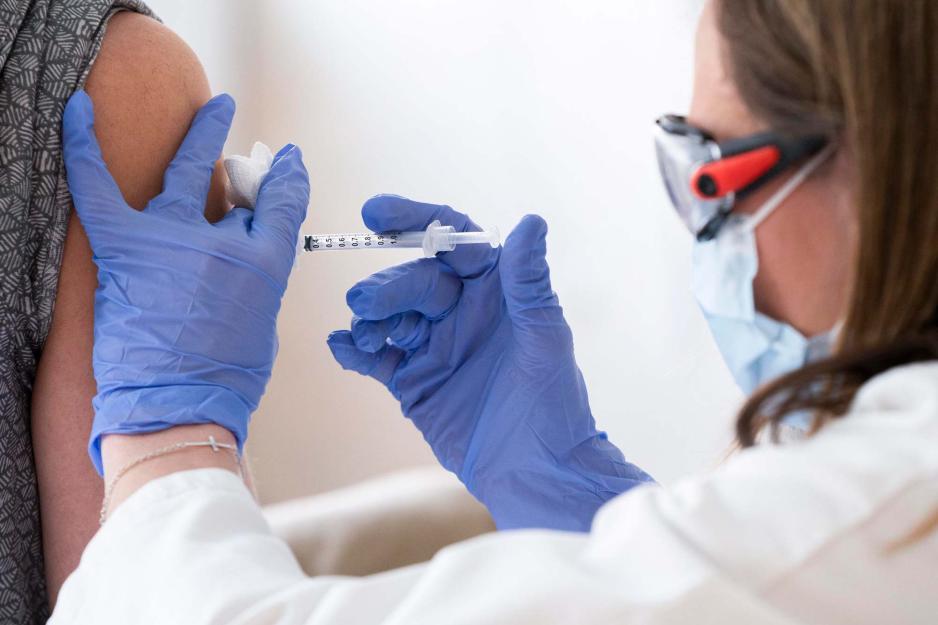 A nurse wearing latex gloves, a mask and goggles administers a COVID vaccine shot in a woman's arm.
