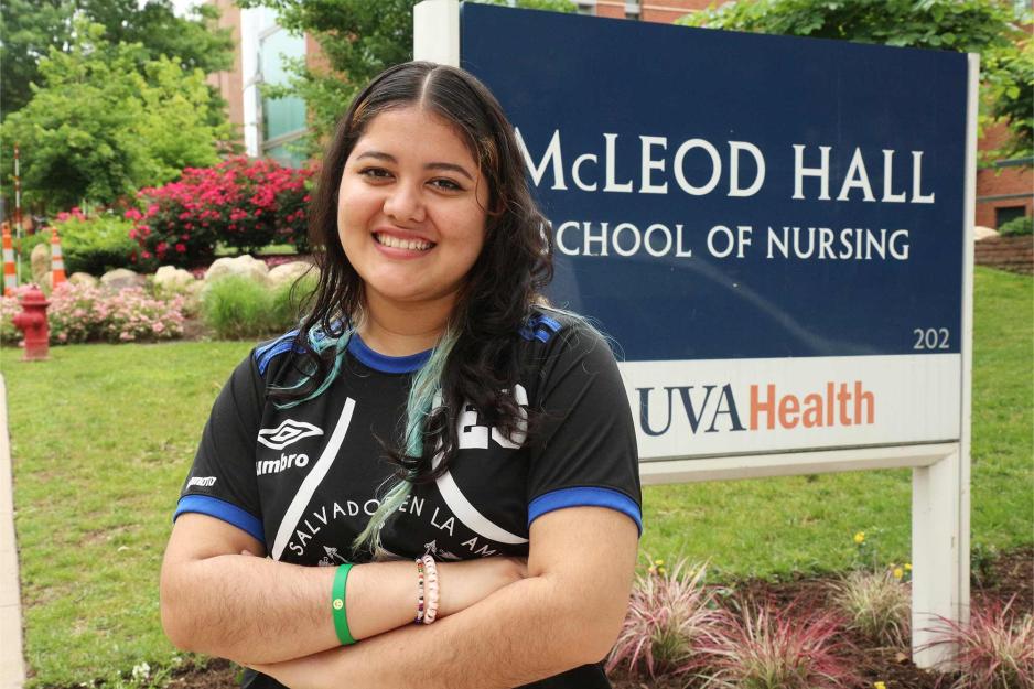 Flores stands in front of a sign reading, 'McLoad Hall, School of Nuring, UVA Health.'