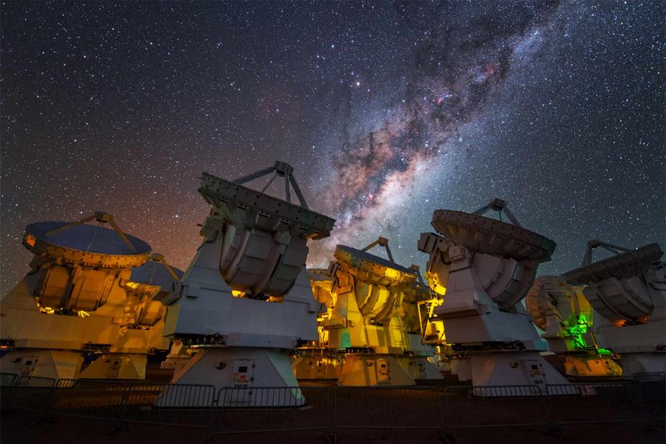 Radio telescopes lit up at night under the Milky Way