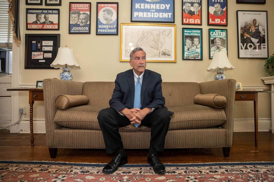 Larry Sabato sits on a couch in an office full of vintage political posters and looks off camera